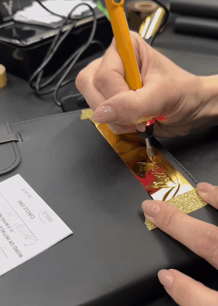 The name Caroline in the process of being foiled on a black journal in calligraphy
